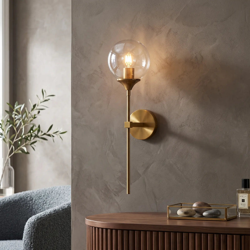 Applique murale style flambeau en métal doré avec globe sphérique en verre transparent au-dessus d'une console contemporaine