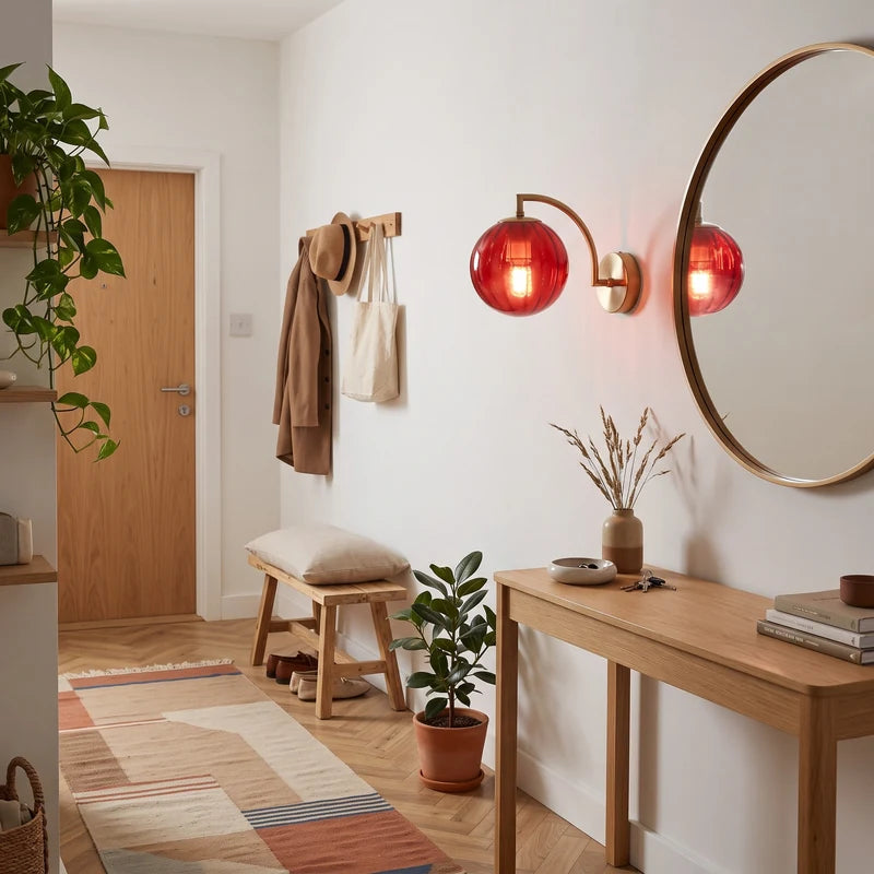 Applique murale globe en verre rouge et métal doré allumée dans une entrée avec miroir rond