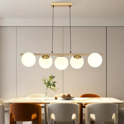 Lustre barre dorée à boules blanches suspendu au-dessus d'une table à manger contemporaine dans une pièce lumineuse
