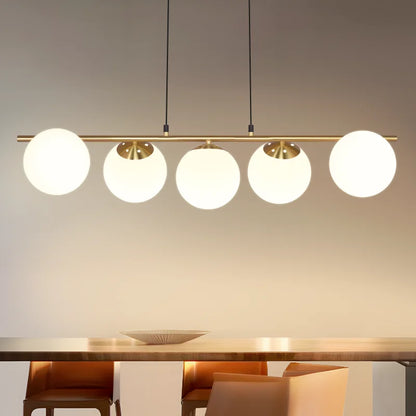 Suspension linéaire moderne à cinq globes en verre blanc opalin et barre en métal doré au-dessus d'une table à manger